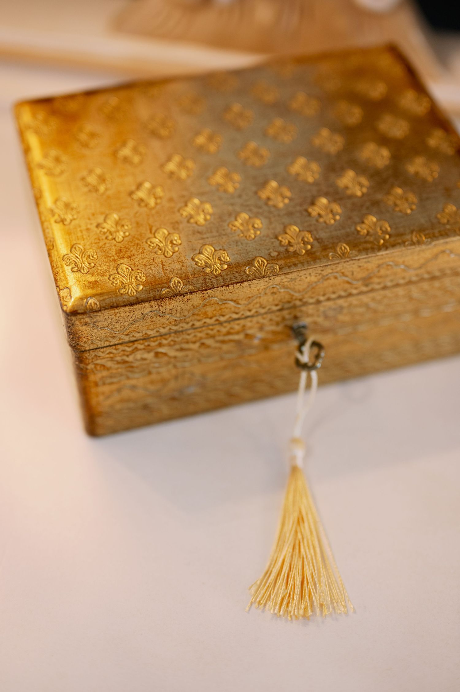 Vintage gold decorative box with floral pattern and yellow tassel detail.
