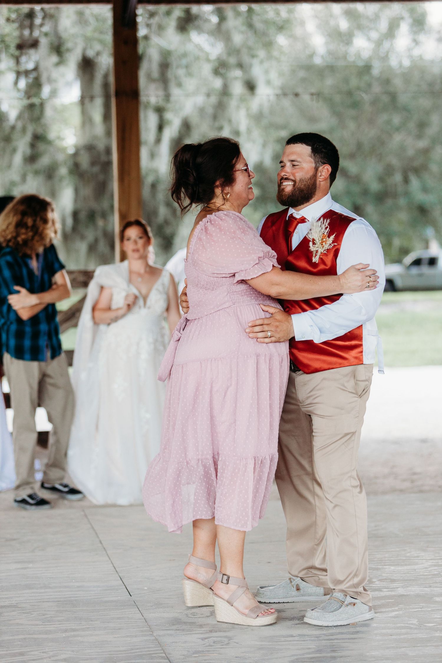 A couple shares a dance in pink and white attire at an outdoor covered venue.