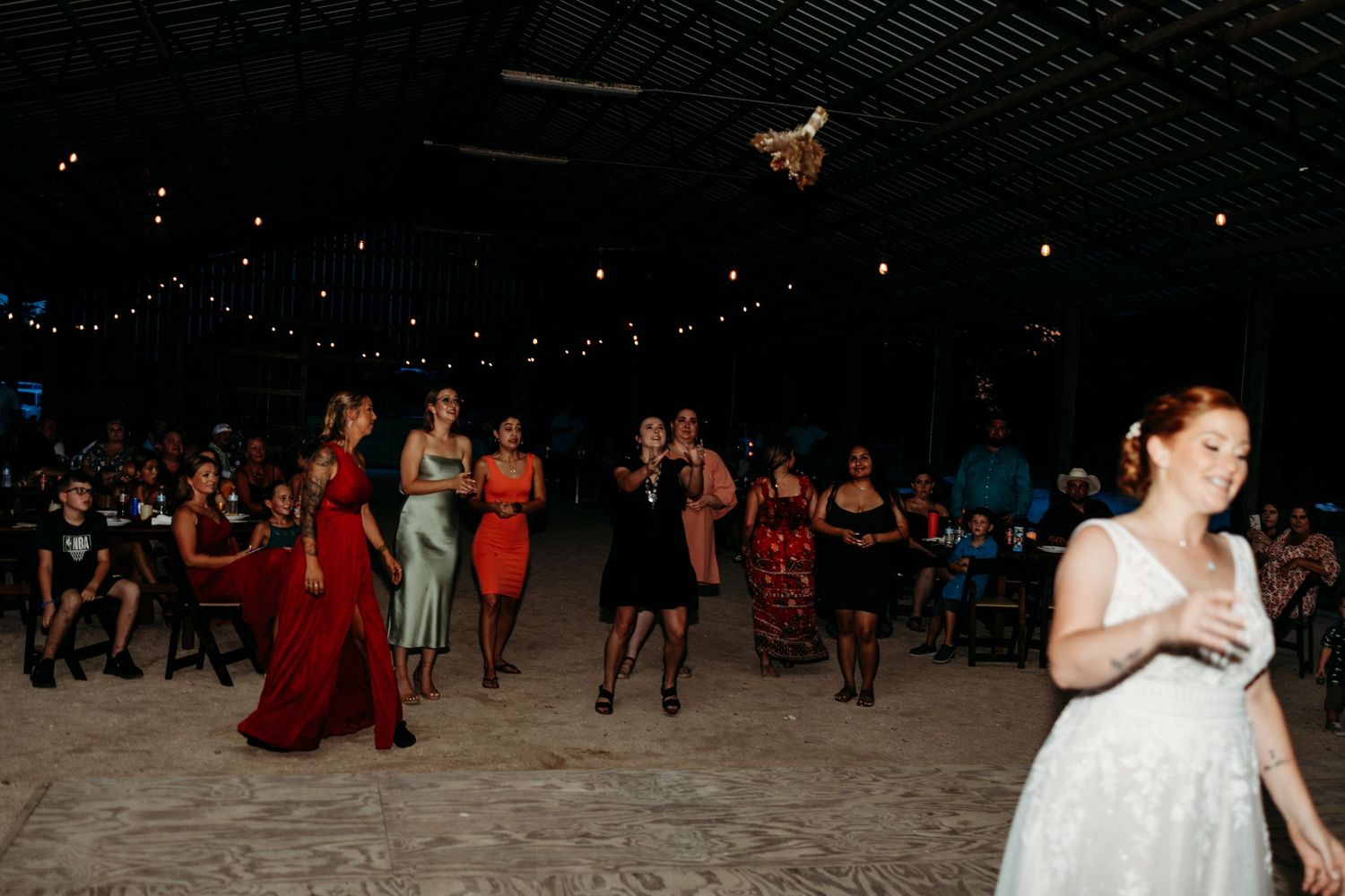 Wedding guests dance on a rustic venue floor while string lights glow overhead.