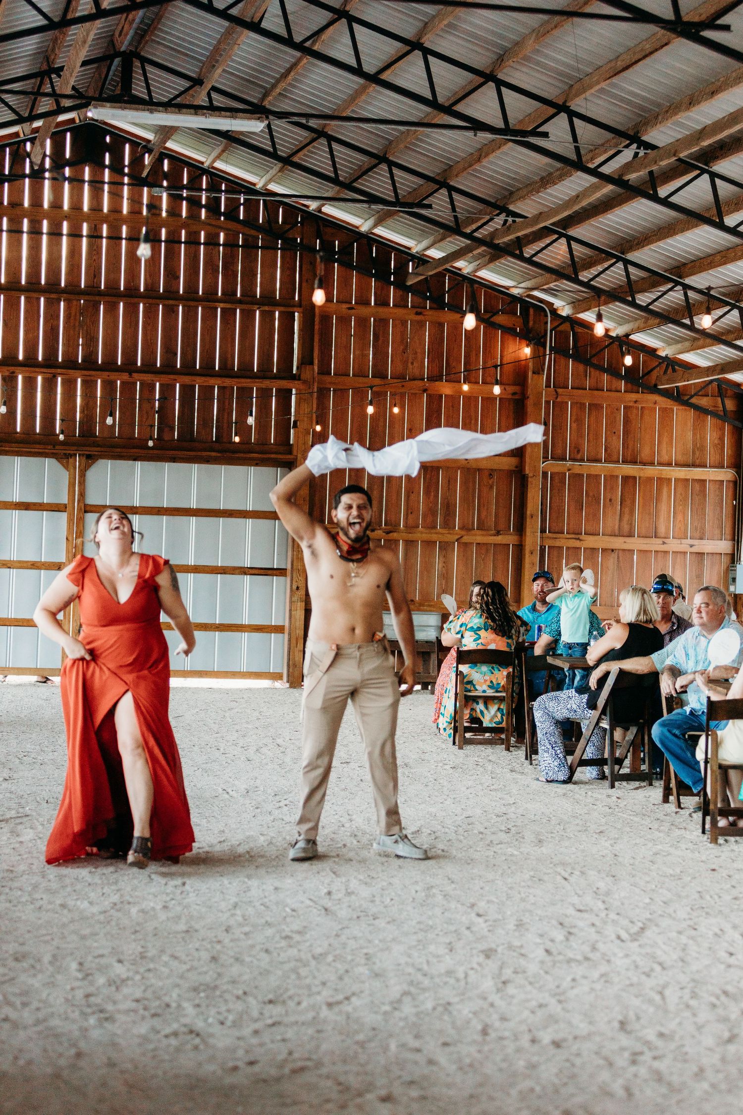 A couple performs a fun dance routine in a rustic barn while guests watch from their seats.