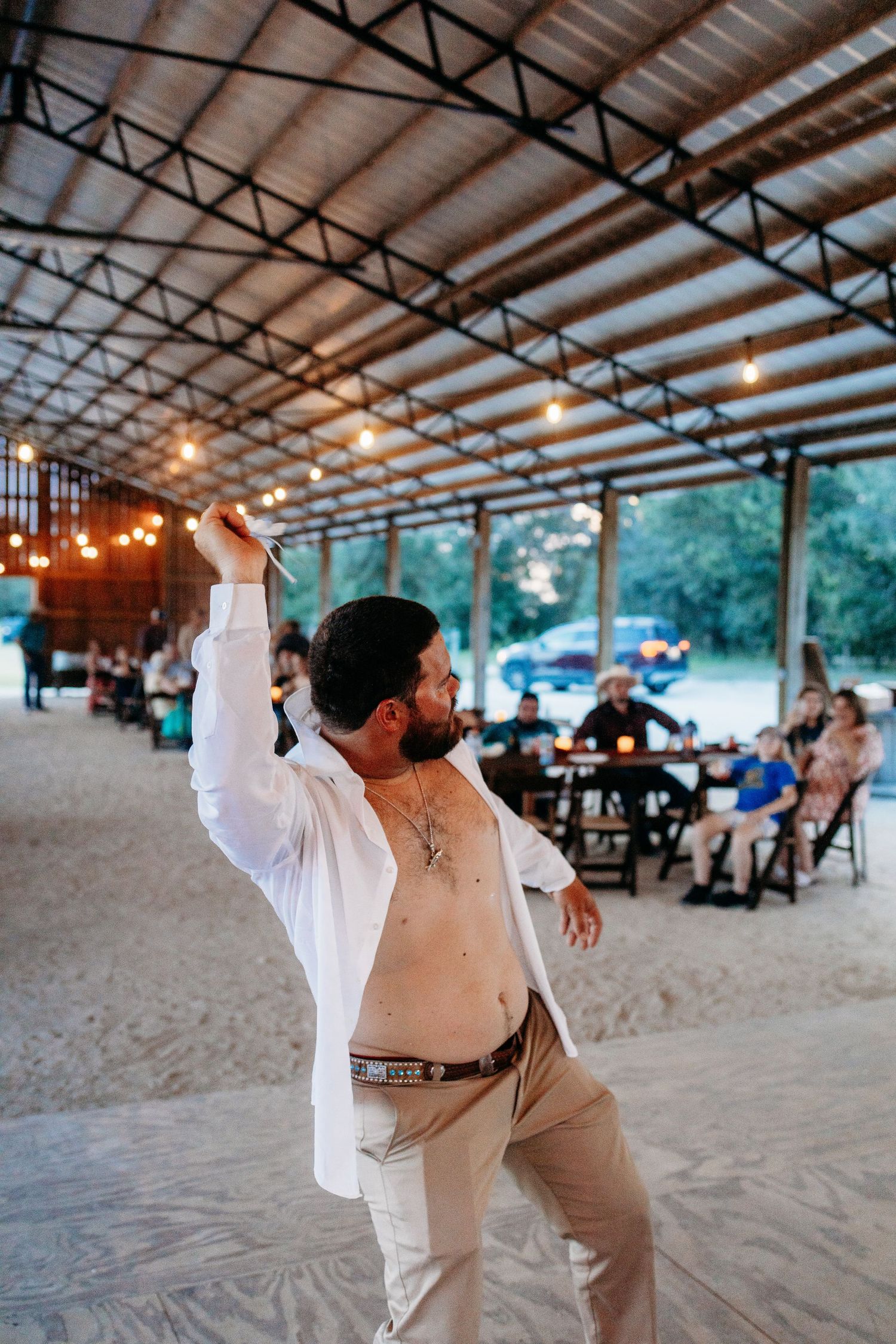 A person dancing in a white shirt and khaki pants under a covered outdoor venue with string lights.
