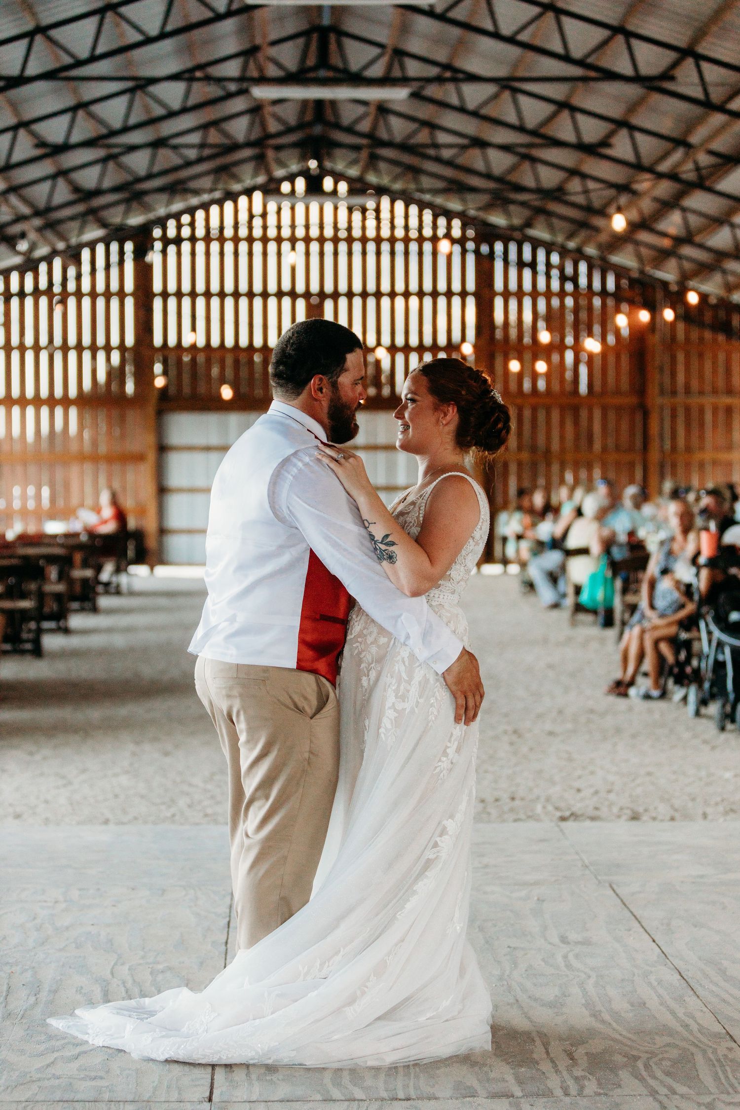 A first dance moment in a rustic barn venue with string lights overhead.