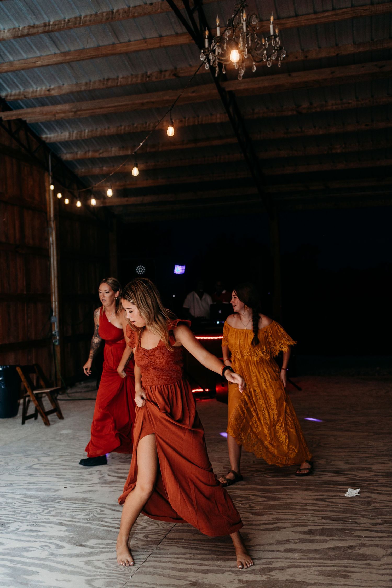 Women in flowing red dresses dance energetically at a wedding reception under string lights.