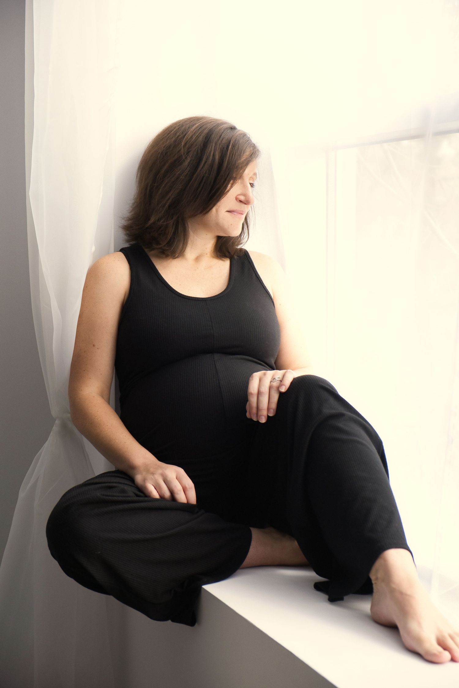 Portrait d'une femme enceinte assise sur le rebord d'une fenêtre. Portrait of a pregnant woman sitting on a window sill