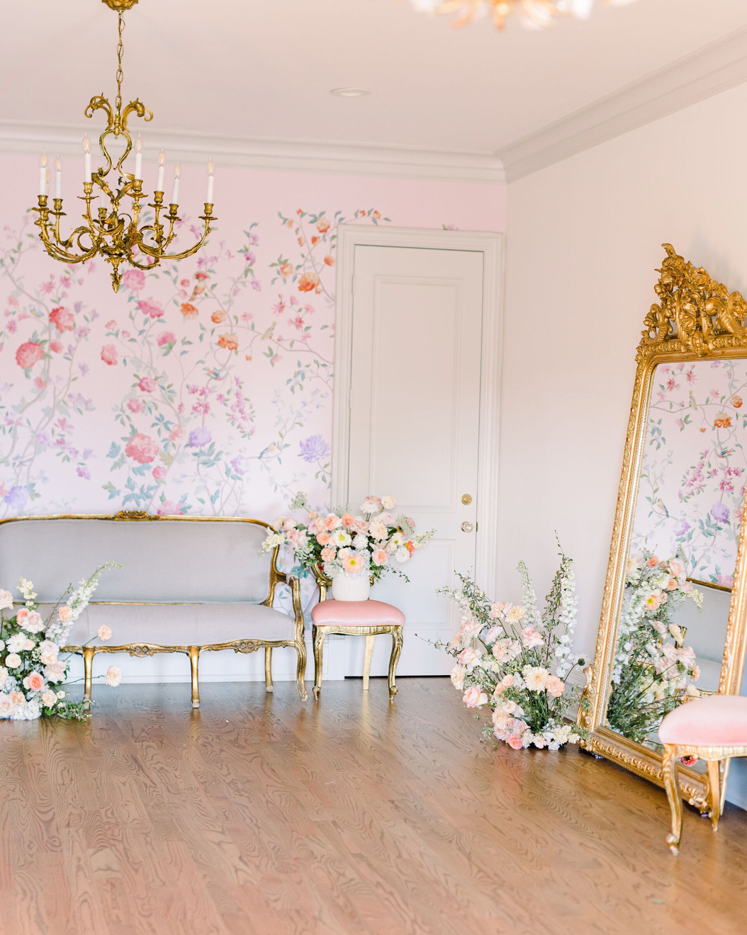 Light and airy photography studio with romantic floral wallpaper, gold mirrors, and hardwood floors.