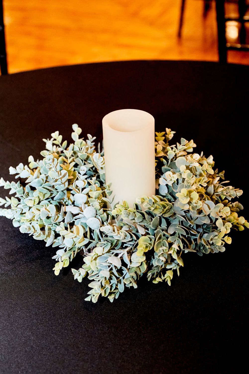 White pillar candle centerpiece surrounded by soft blue-green eucalyptus on black tablecloth.