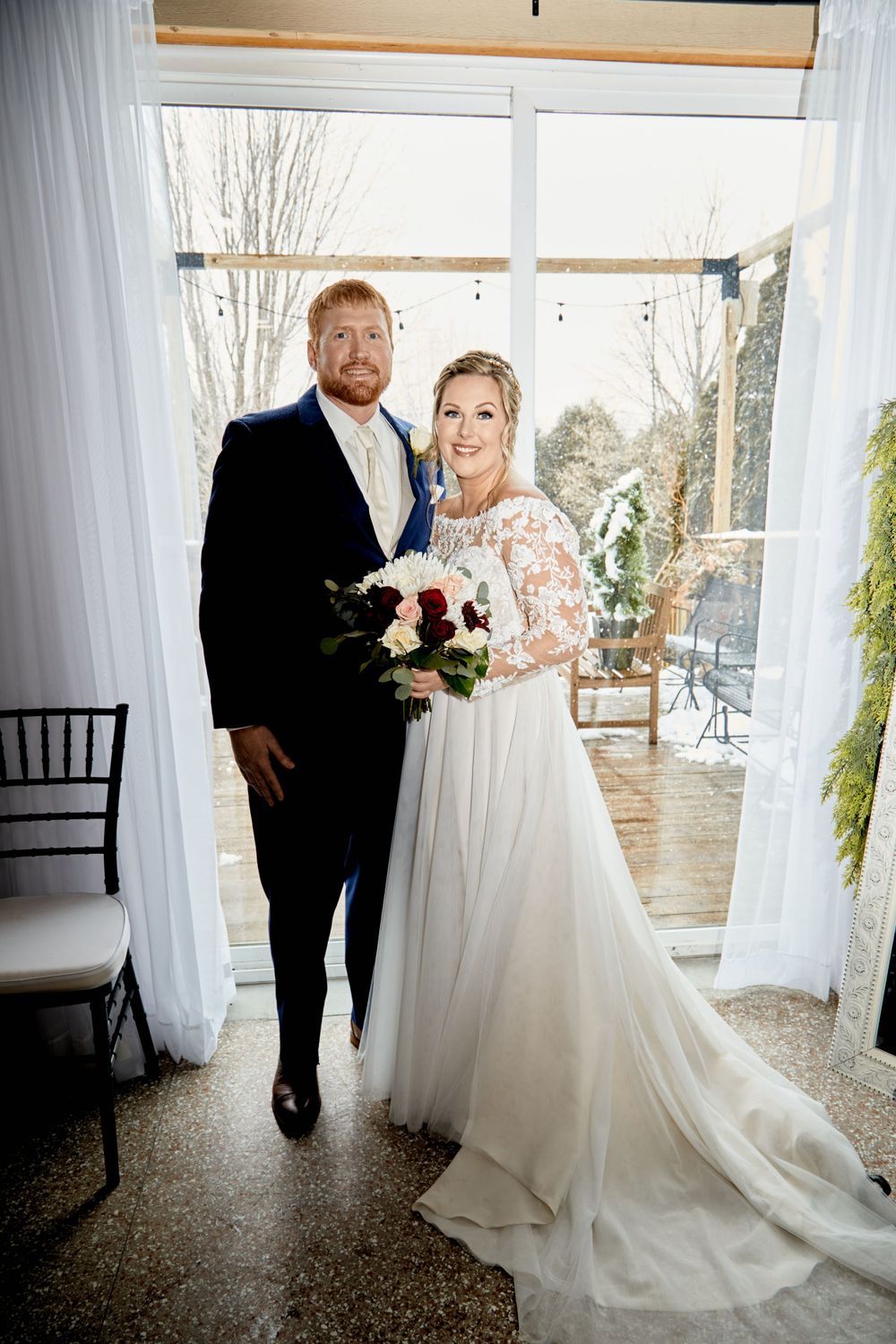 Wedding couple poses in elegant venue with white drapes and natural lighting.