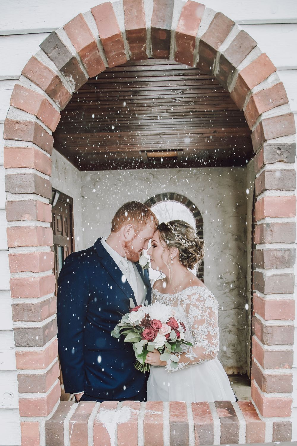 Romantic wedding portrait in brick archway with falling snow effect.