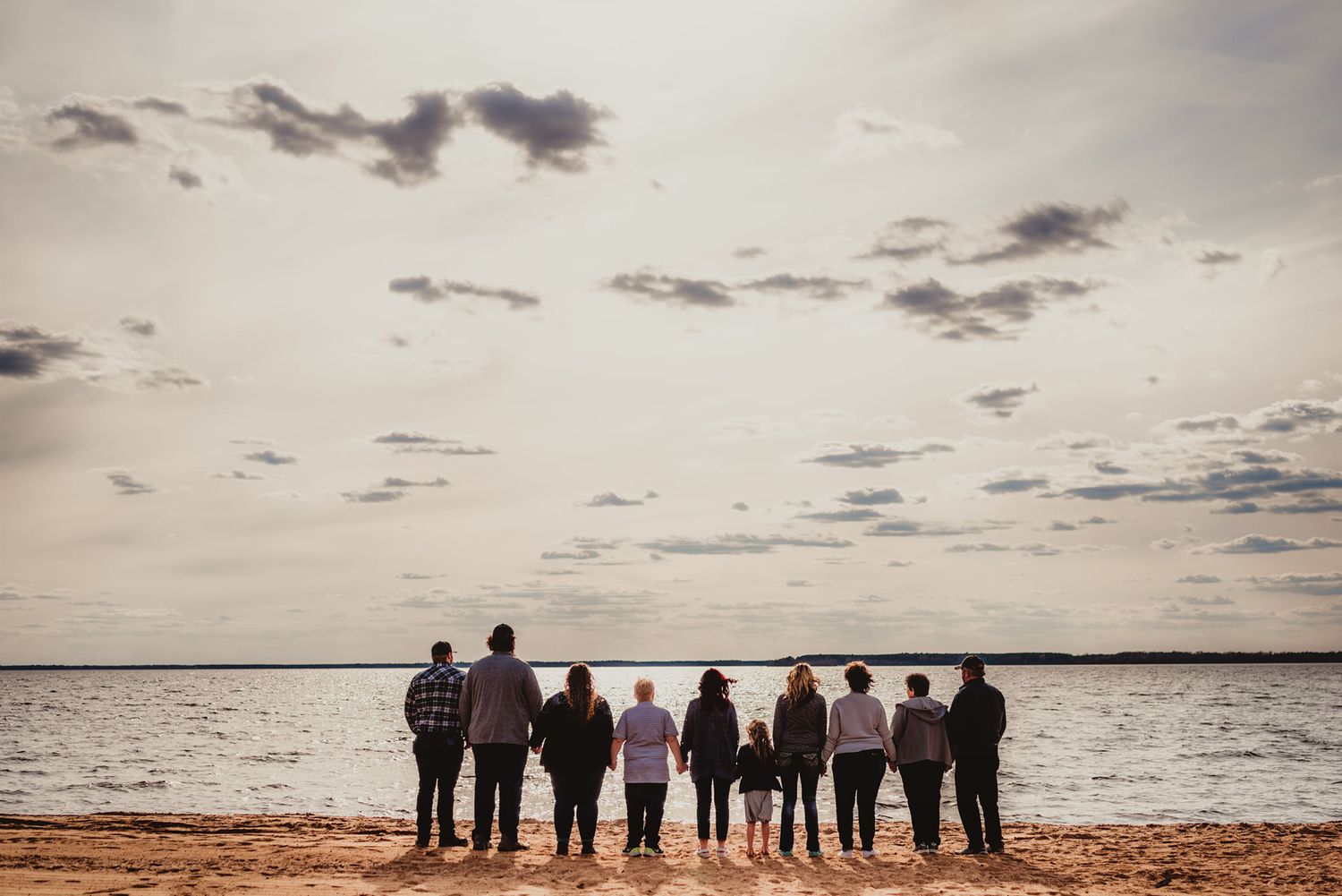 Silhouette of a large group standing together against a dramatic sunset sky over water.