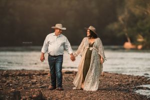 Romantic couple walking along rocky beach shoreline at sunset.