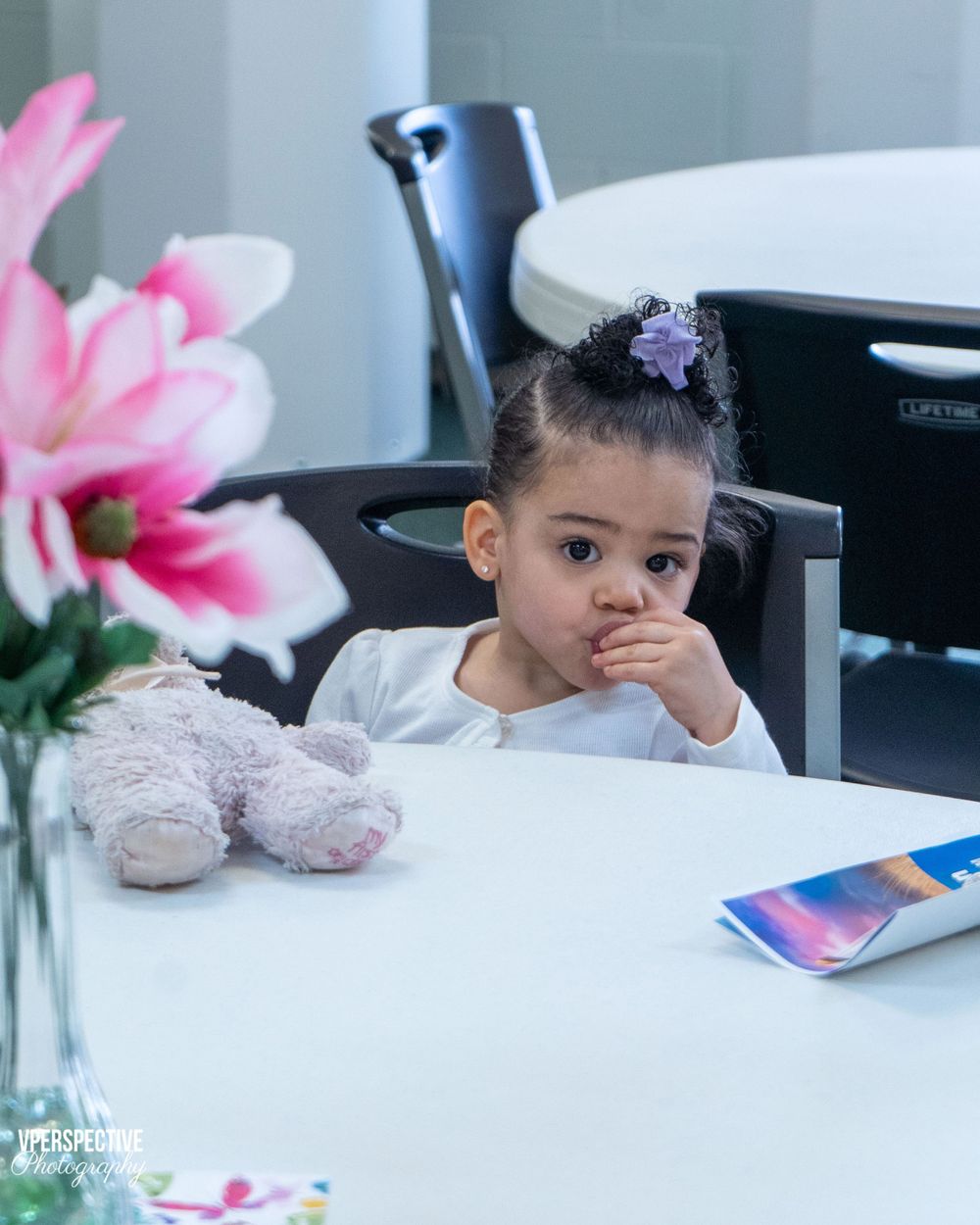 Young child sits at desk with pink flowers and stuffed animal.