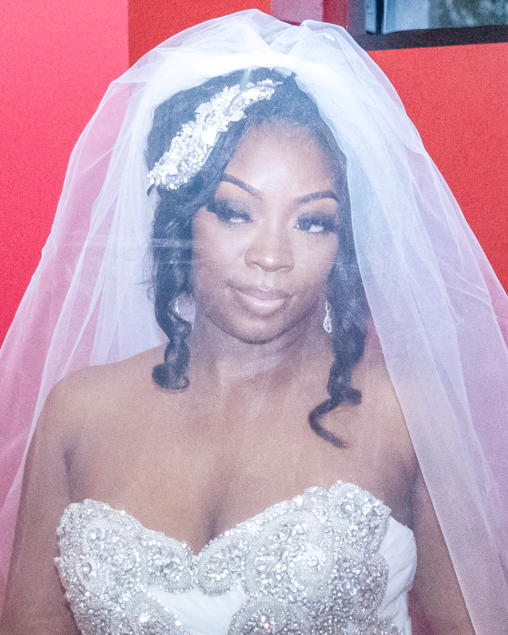Stunning bride wearing crystal-embellished gown and veil against pink background.