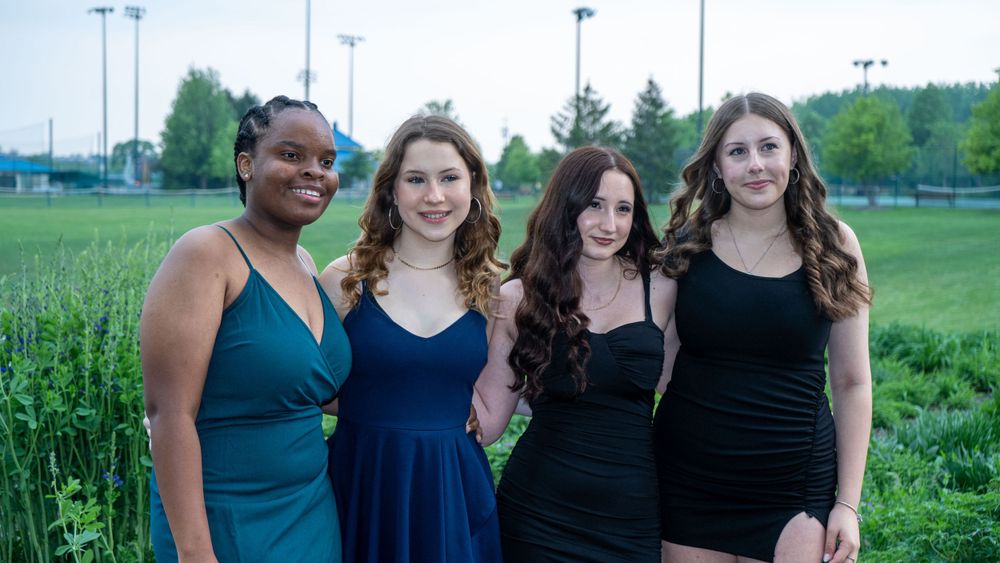 Group of friends in formal dresses pose together outdoors at dusk.