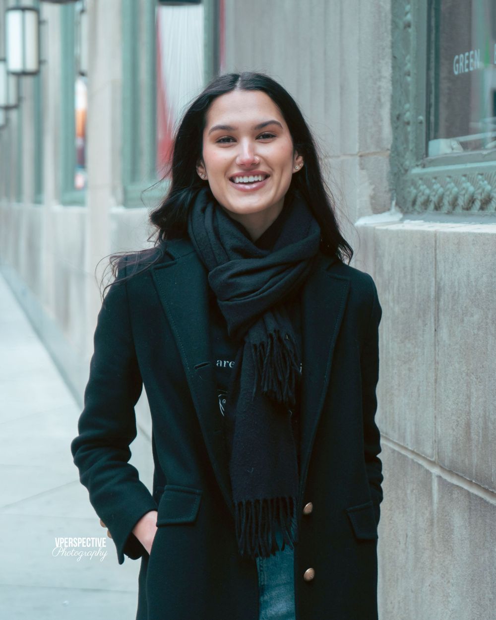 Winter portrait of person in black coat and scarf on city street.