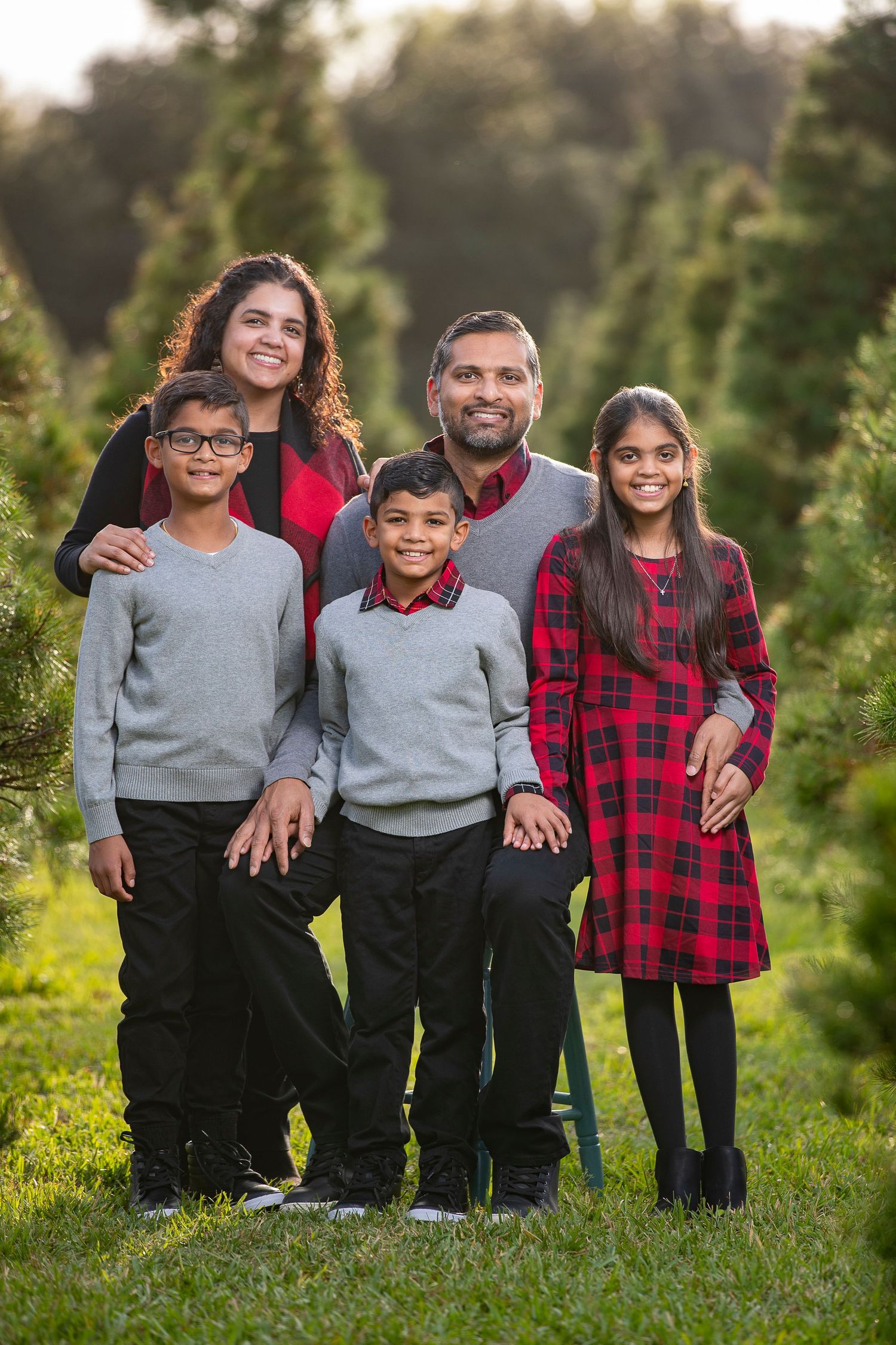Family portrait of five people standing together among evergreen trees.