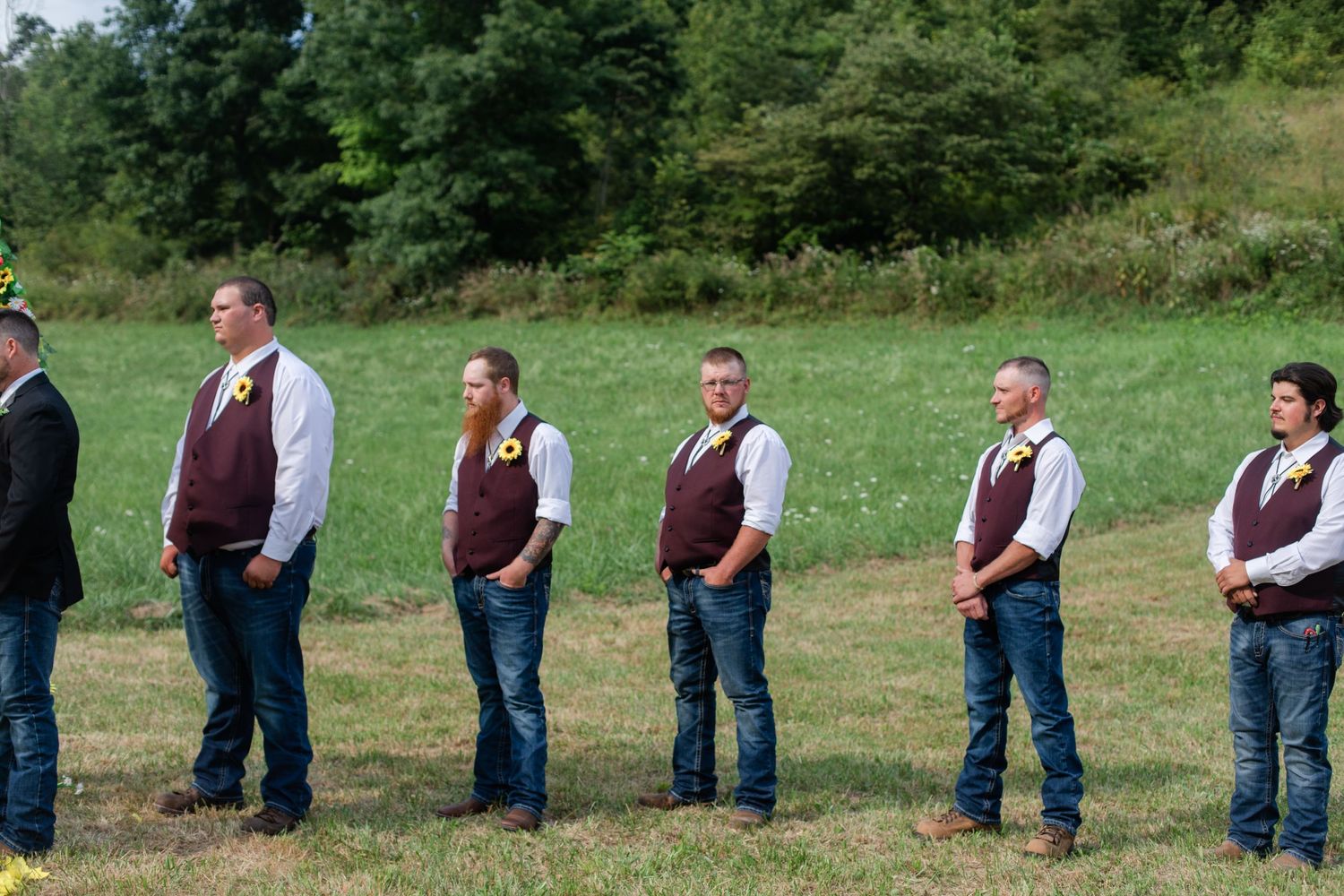 Wedding ceremony participants arranged in line formation on rolling green hillside.