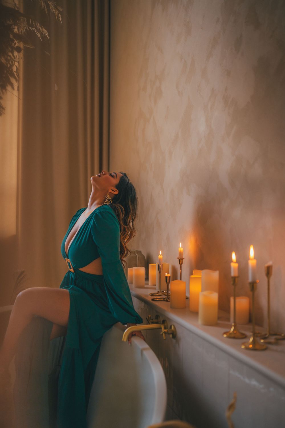 Woman in emerald green dress relaxes in candlelit bathroom with romantic ambiance and soft lighting.