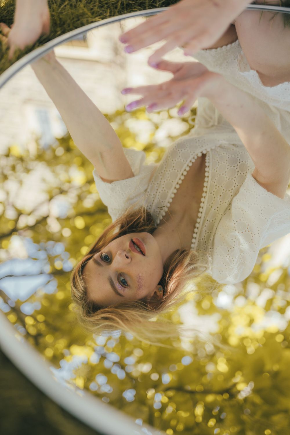A dreamy reflection captured in a circular mirror outdoors with sunlit golden bokeh in the background.
