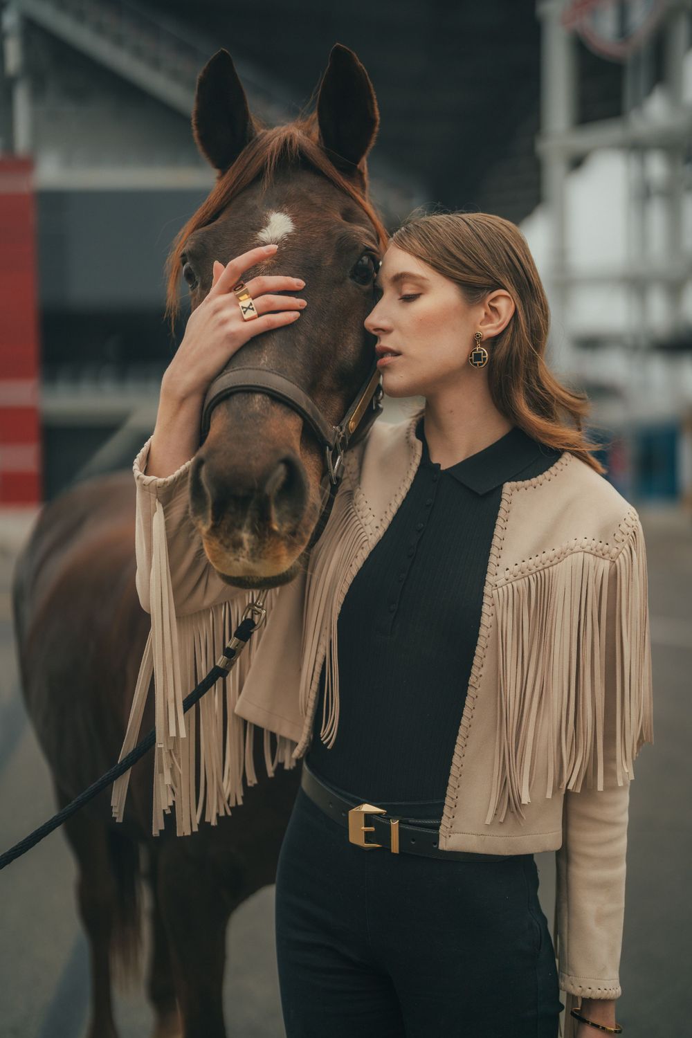 Moody fashion portrait with a beautiful brown horse and model wearing a fringed jacket.