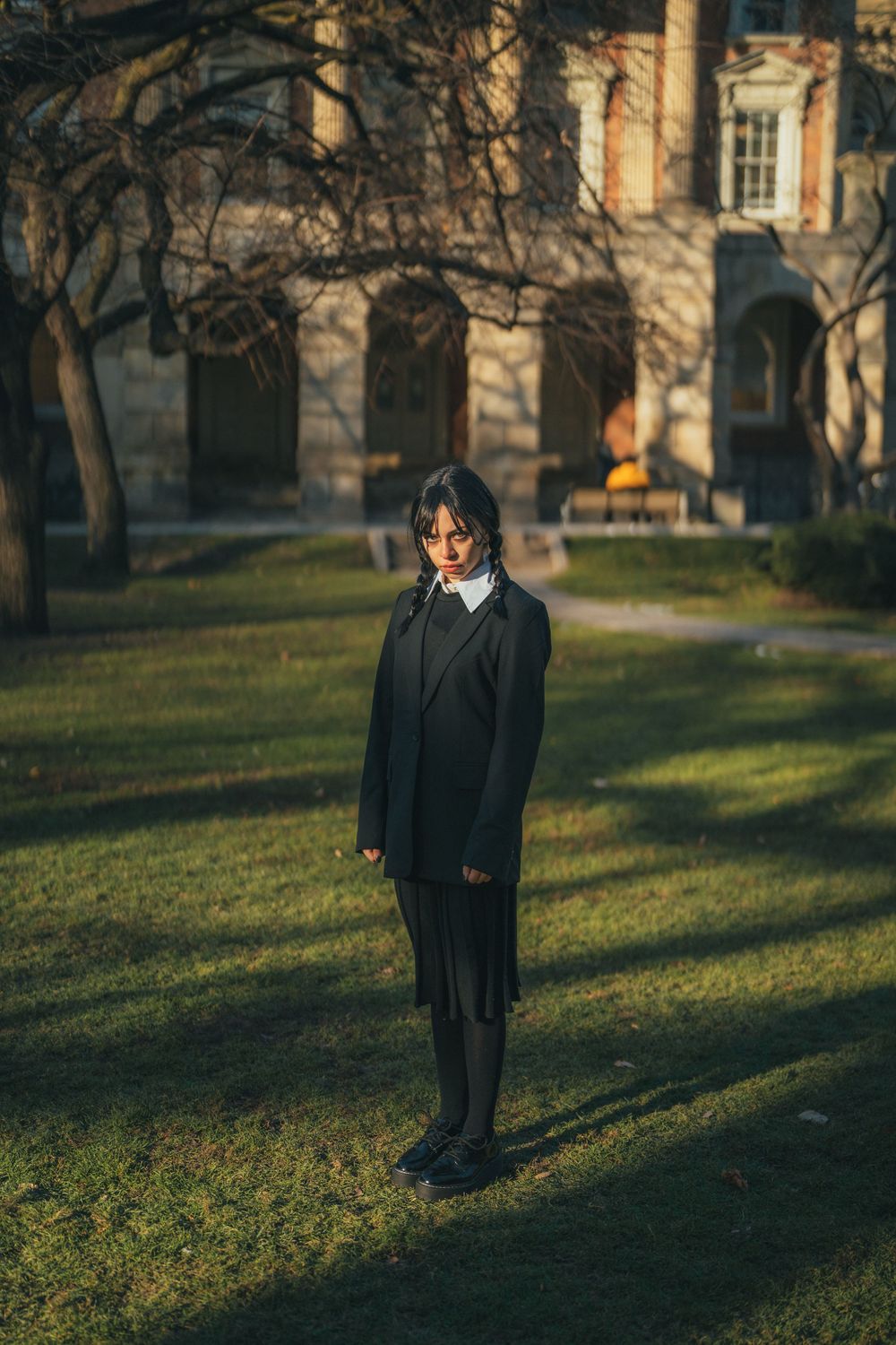Portrait in formal attire standing on grass with historic architecture in late afternoon light.