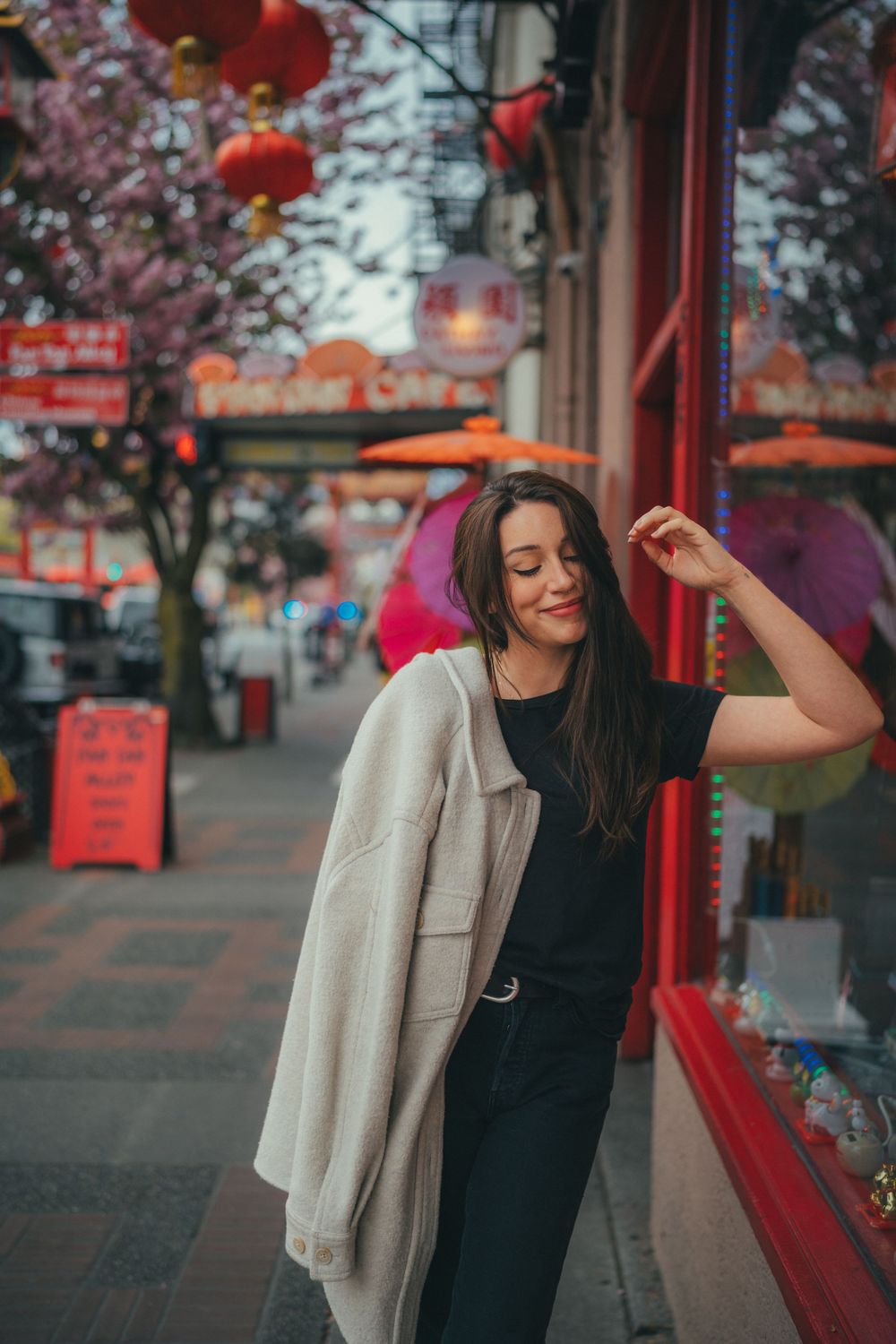 A candid street scene with red lanterns and cherry blossoms, featuring a casual outfit with beige coat against a storefront.