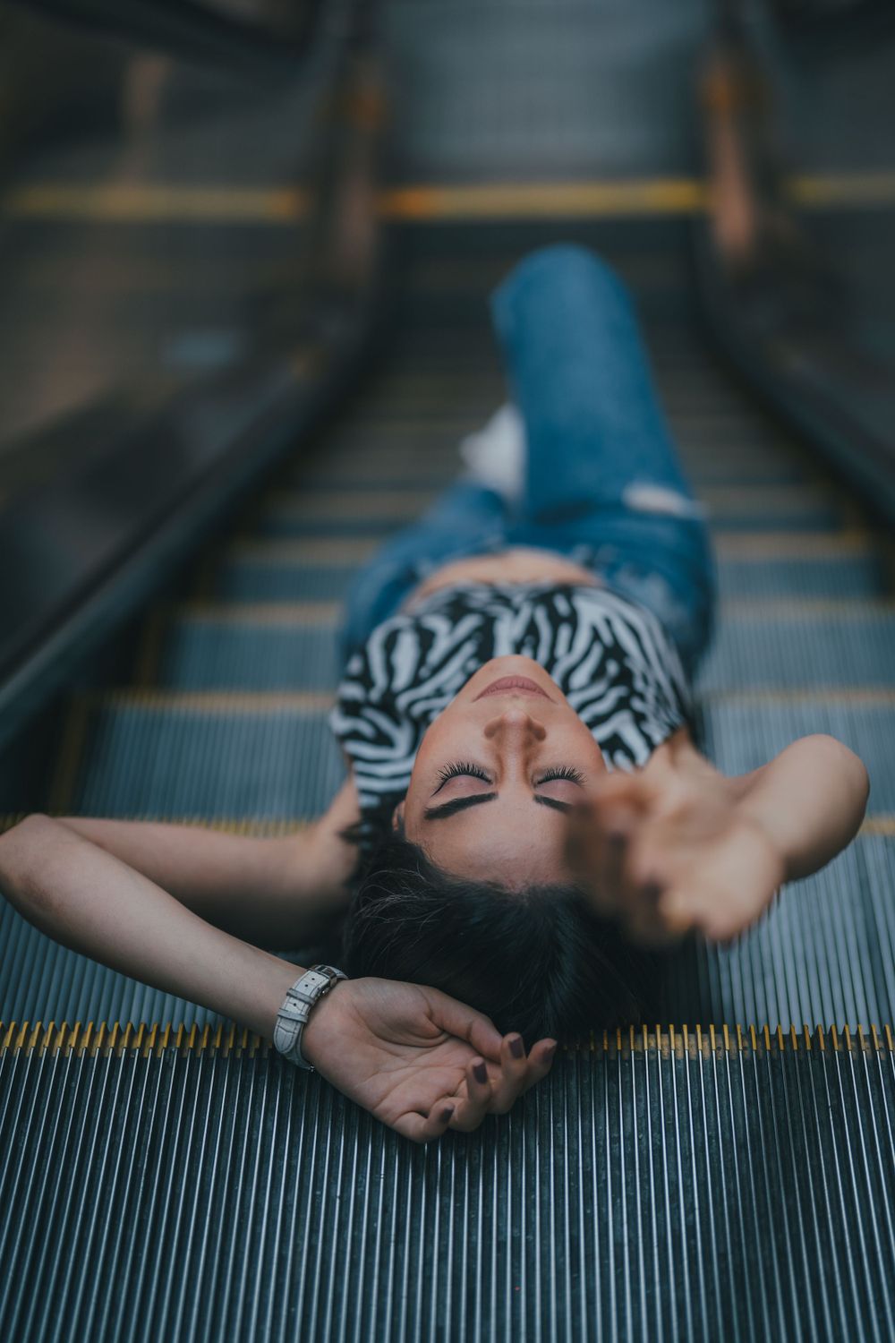 Someone wearing a striped shirt lies on an escalator in a moody urban setting.