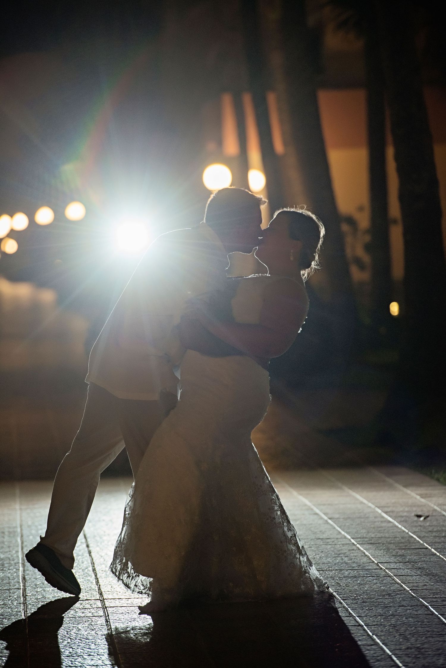 Silhouette of dancing couple backlit by string lights at night.