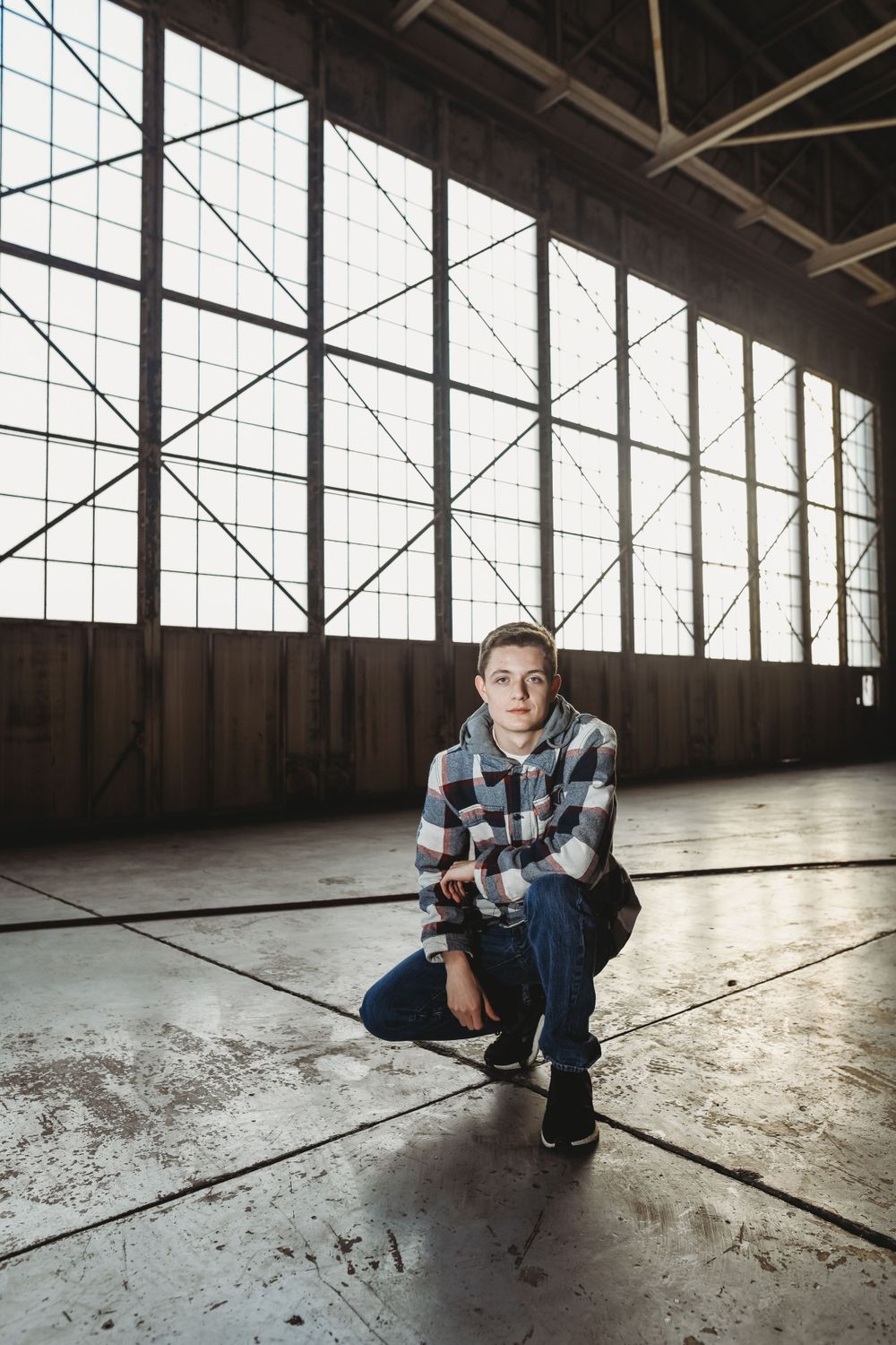 Person crouching in an empty industrial space with large windows.