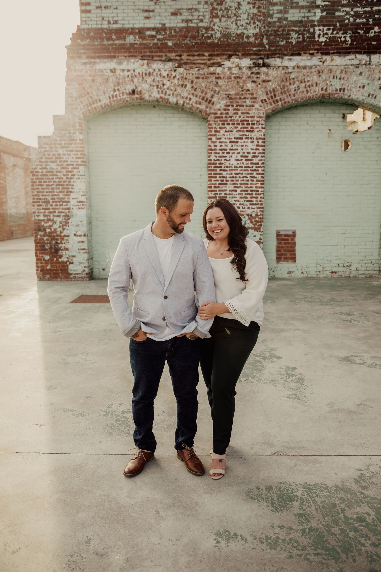 A candid moment between a couple posing against an industrial brick wall backdrop.