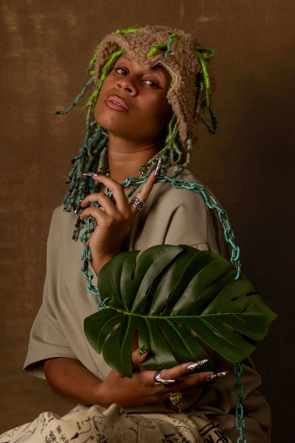 Artistic portrait with a person holding a large monstera leaf in a neutral-toned studio setting.