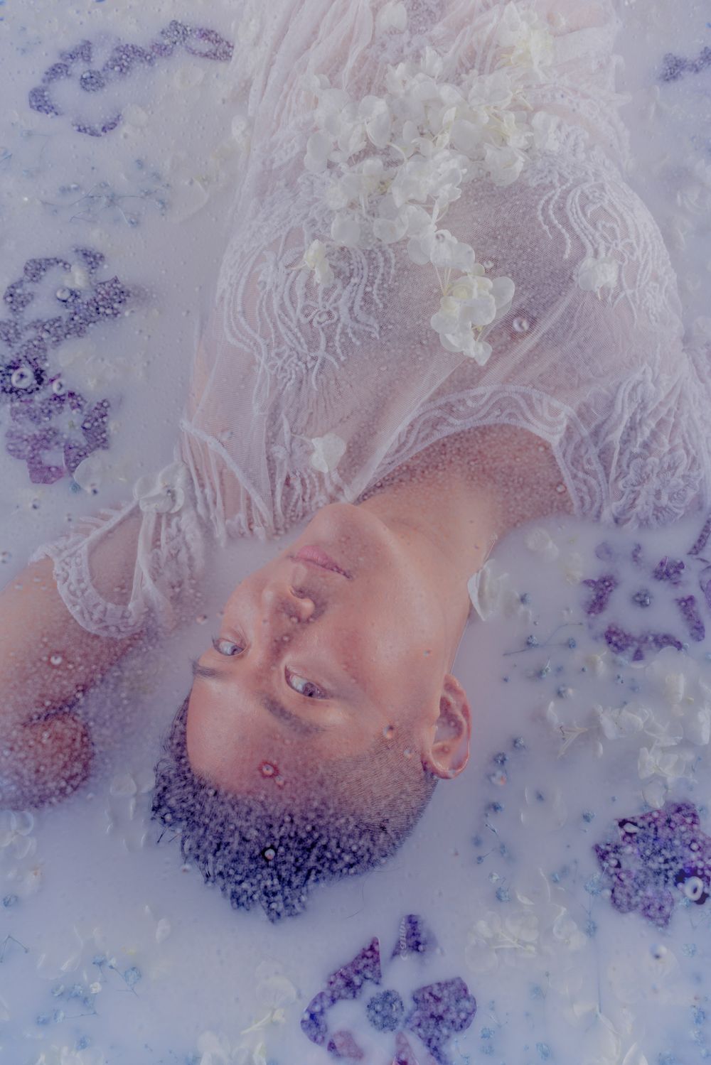 Dreamy portrait in milky water with lace details and purple flower petals.