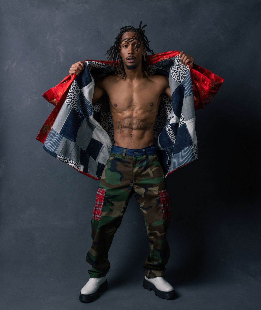 Athletic figure in camouflage pants and jacket poses against dark background.