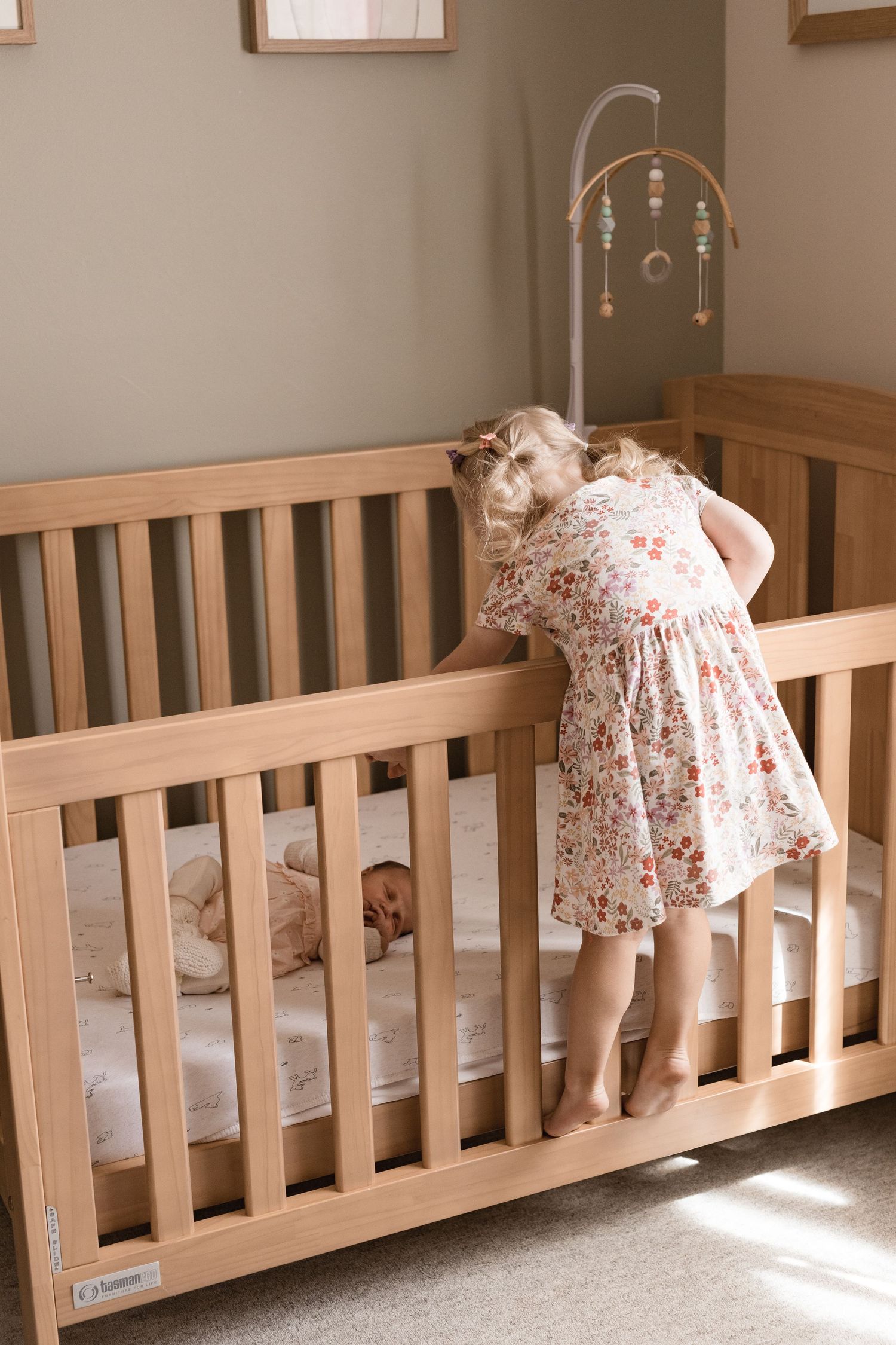 In home newborn session, big sister leaning over cot and looking at her newborn baby sister.