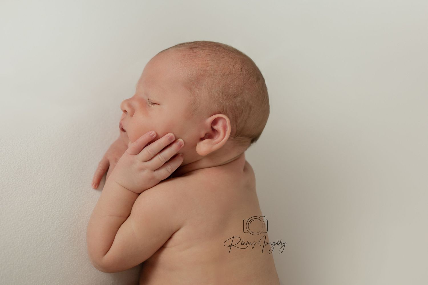 Close-up profile of sleeping newborn baby with hand resting gently against cheek.