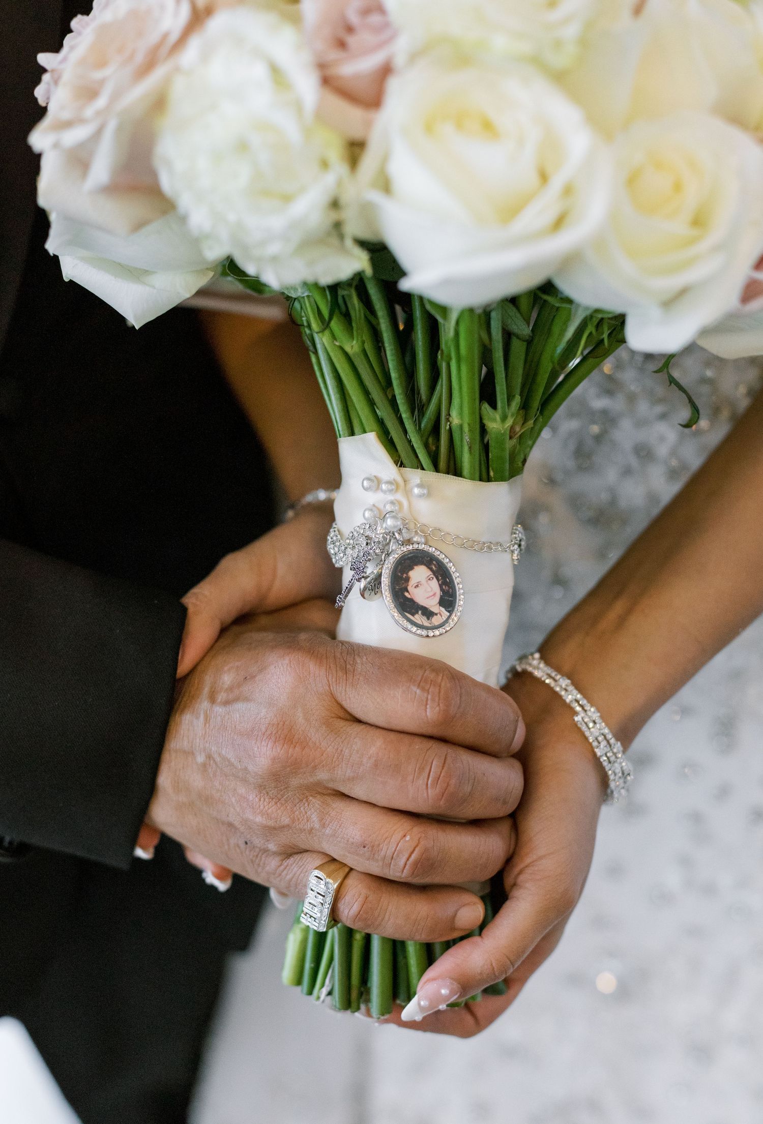 A bridal bouquet of white roses wrapped in lace with a vintage cameo brooch pin detail.