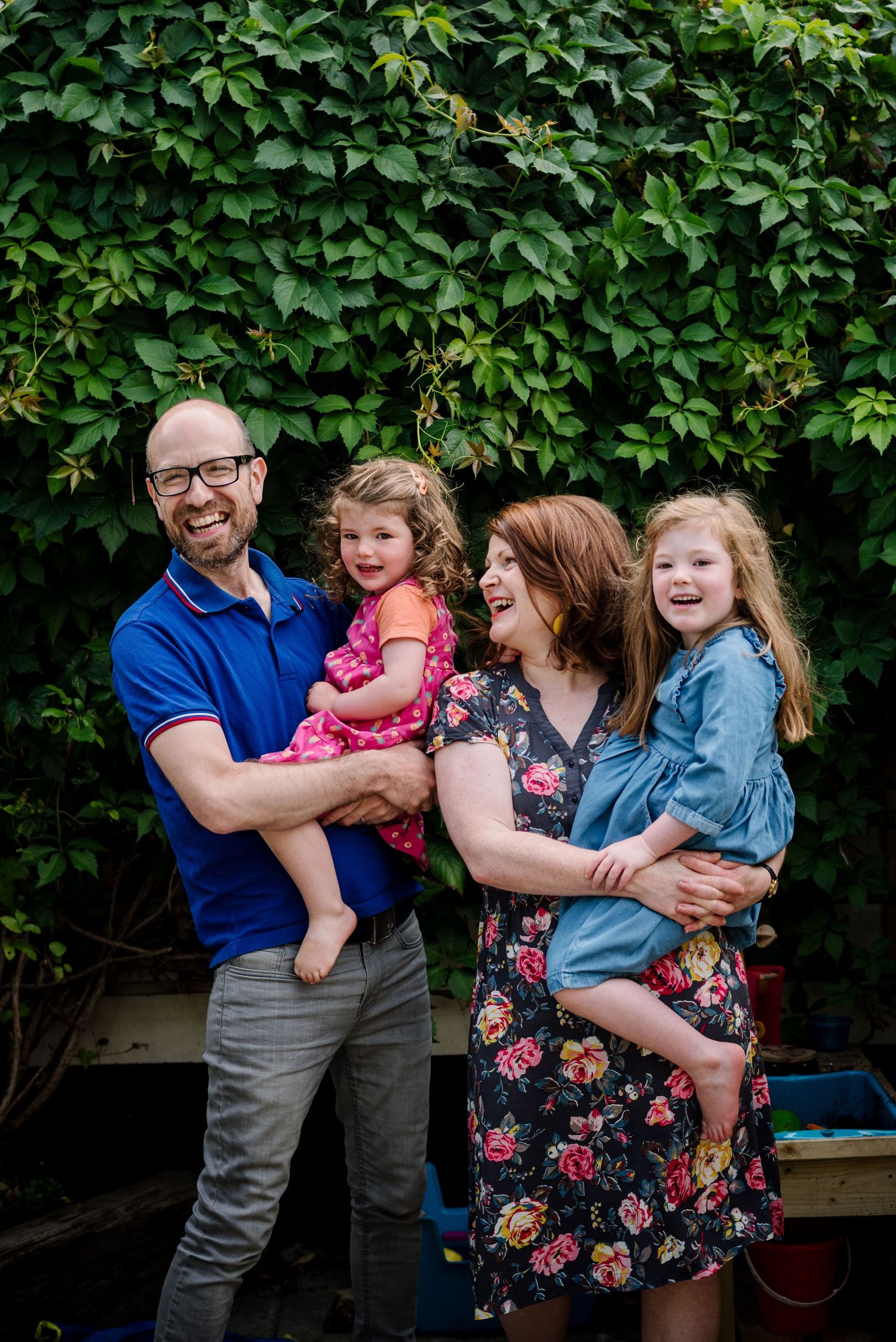 Happy family portrait against lush green hedge background.