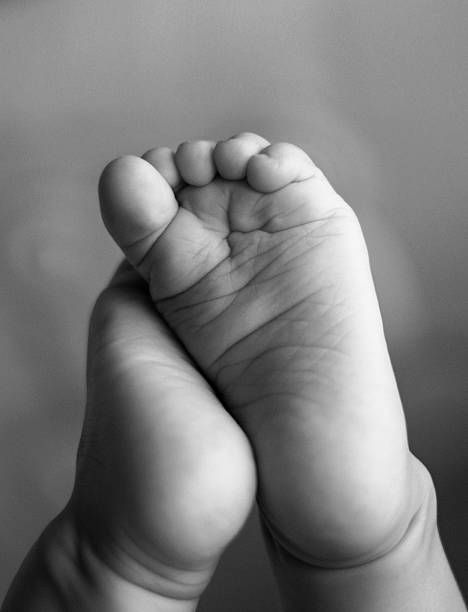 Close-up black and white photo of a tiny baby foot with delicate wrinkles and curled toes.