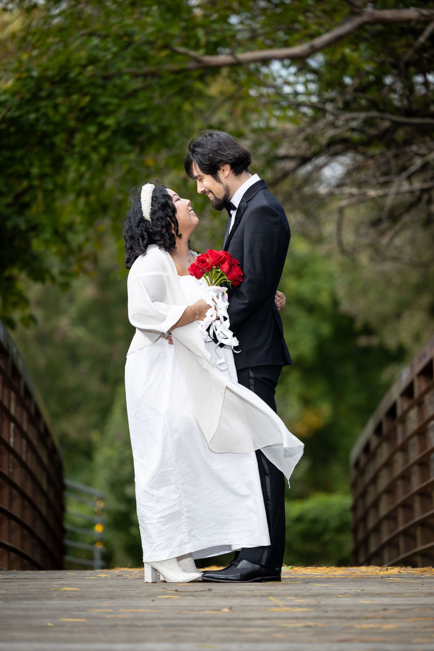 A romantic wedding moment captured on a wooden bridge with fall foliage in the background.