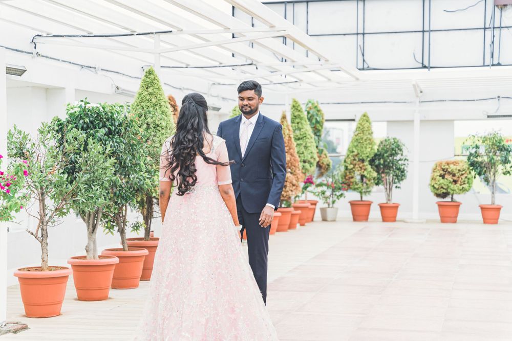 Couple in formal wear standing among decorative potted plants in an indoor venue.