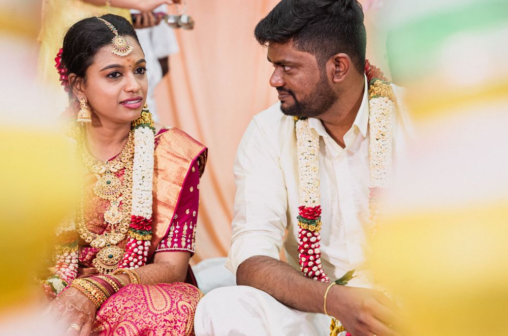 Couple in traditional Indian wedding attire seated during ceremony with floral decorations.