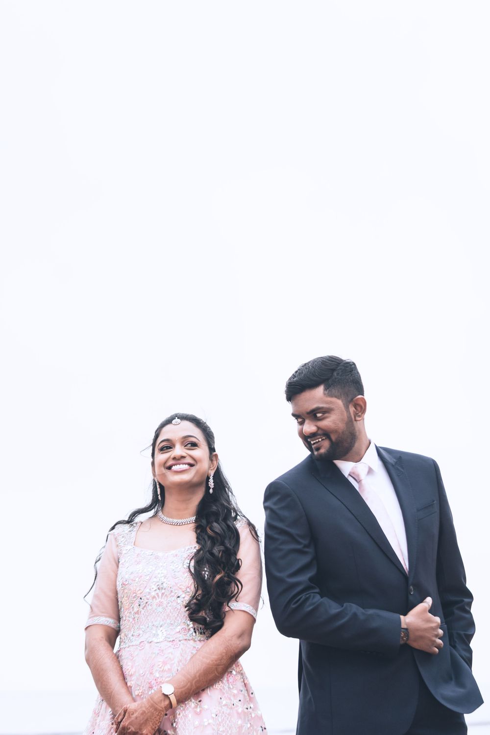 A couple in formal attire share a candid moment against a white background.