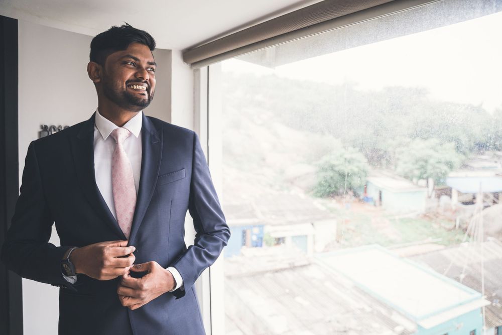 A person in a navy suit adjusts their jacket while standing by a window with a scenic view.