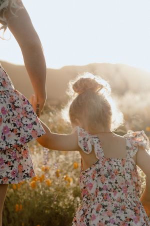 Matching floral dresses silhouetted against golden sunlight in a meadow.