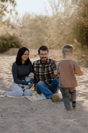 A relaxed family scene on sandy ground with desert brush in the background.