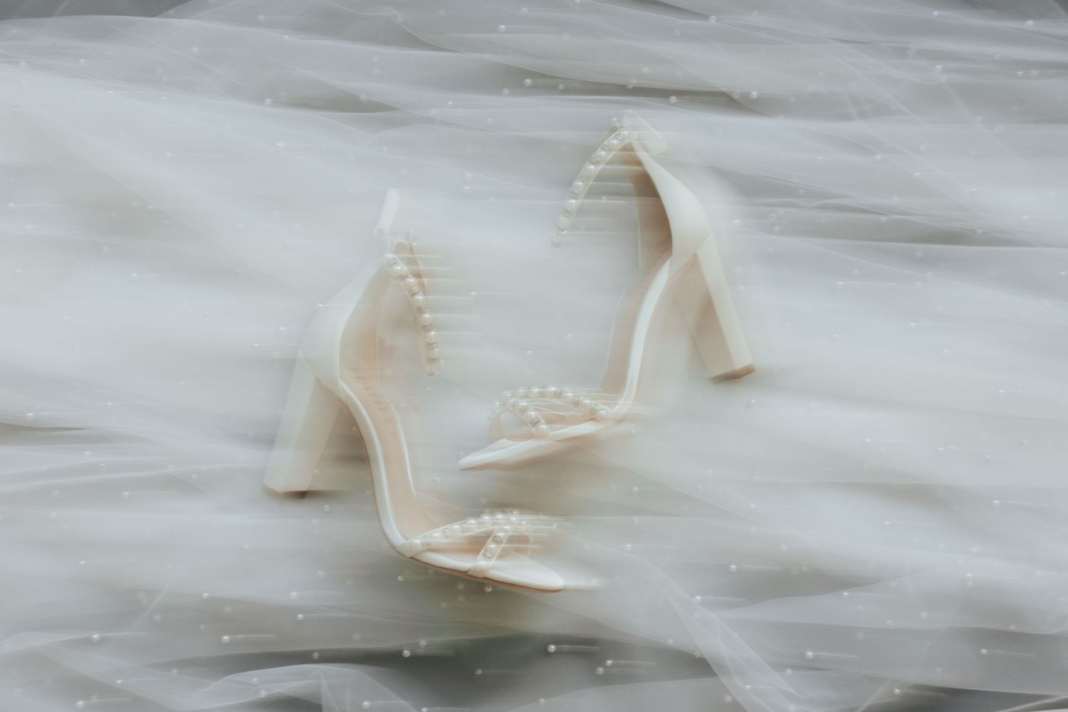 A pair of elegant white high heels with delicate details sit on a marble surface.