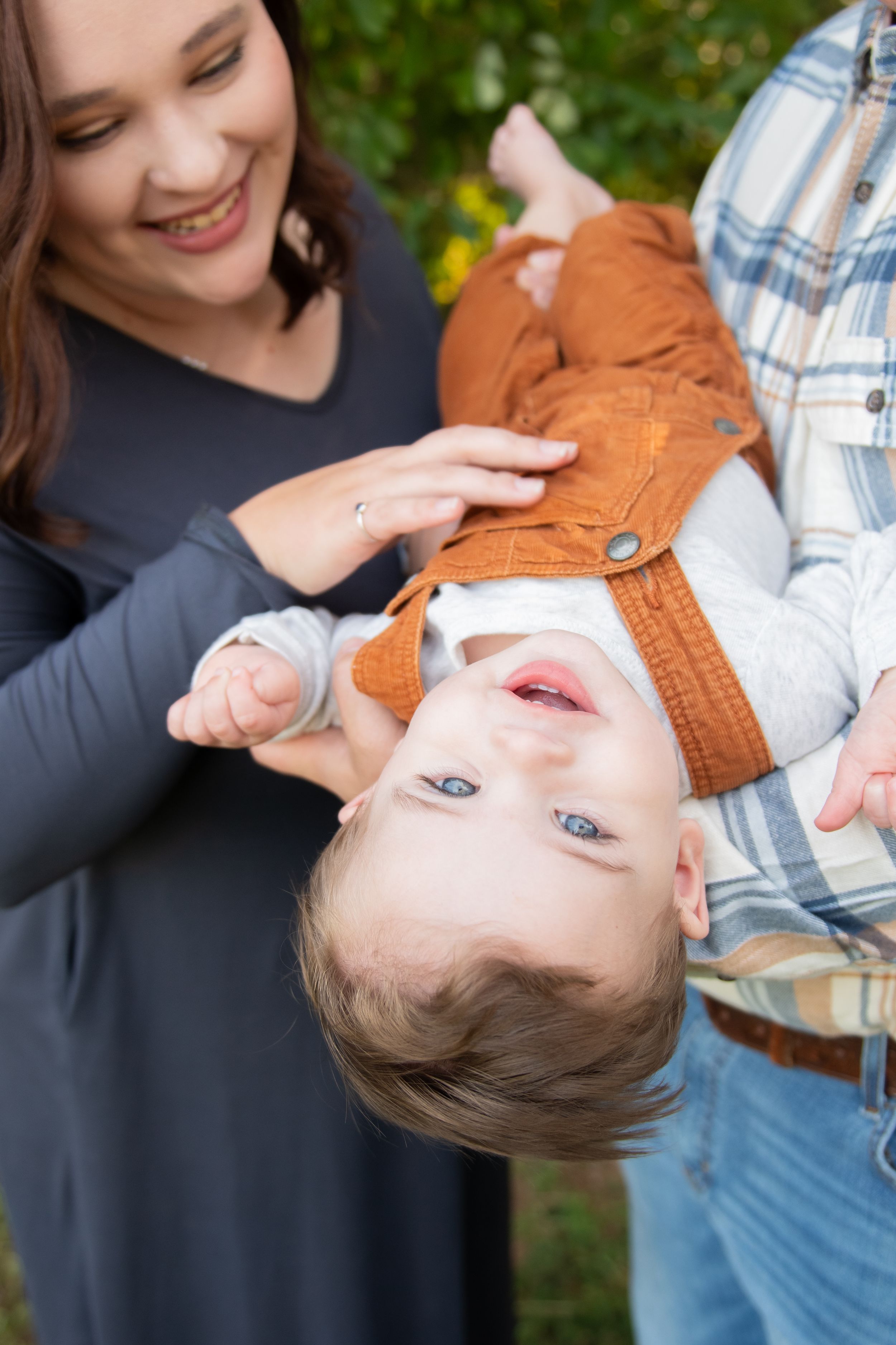 Playful moment captured of a young child being held upside down outdoors with laughter and joy.