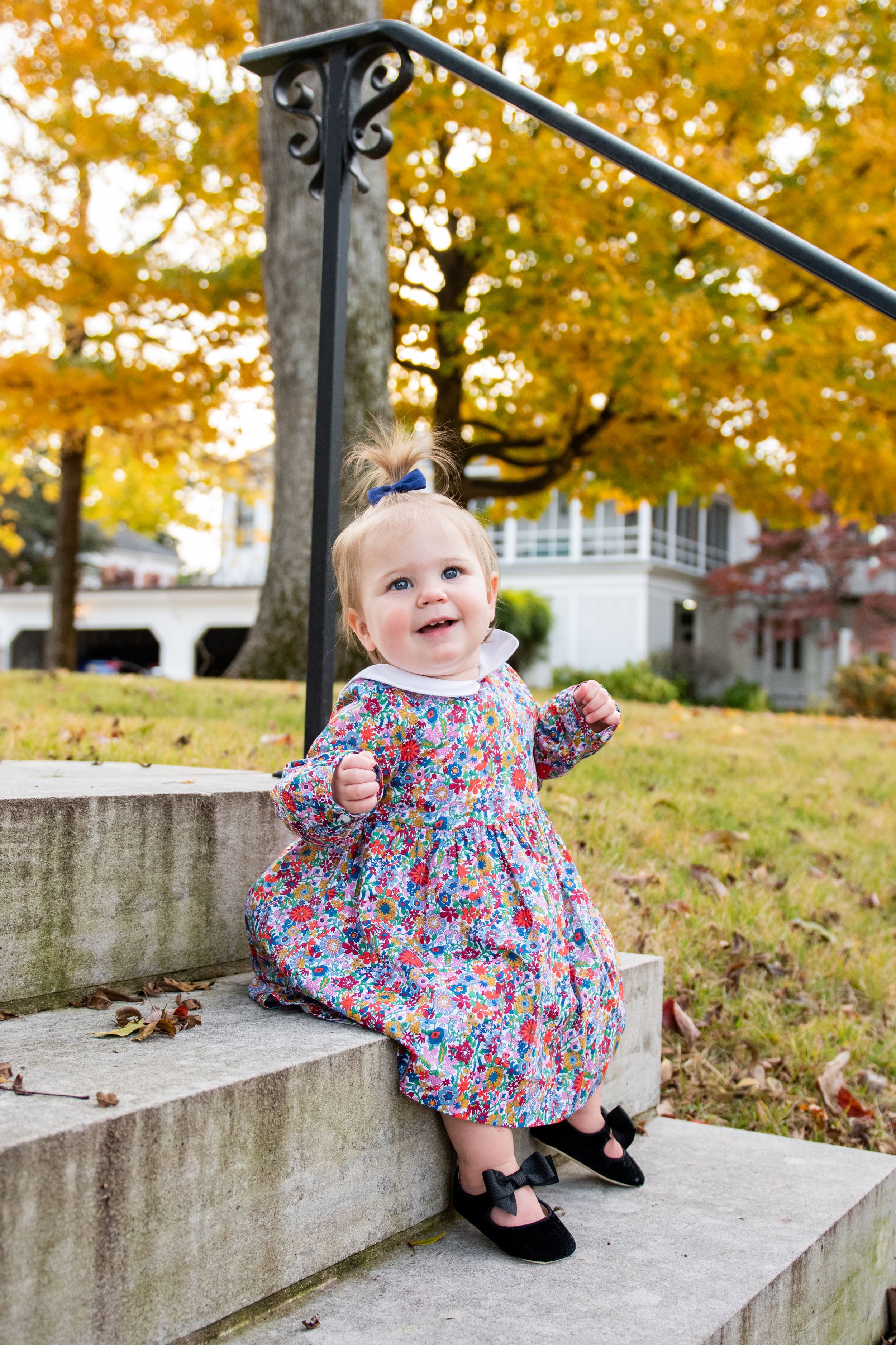 A small child in a floral dress crawling on concrete steps during autumn.