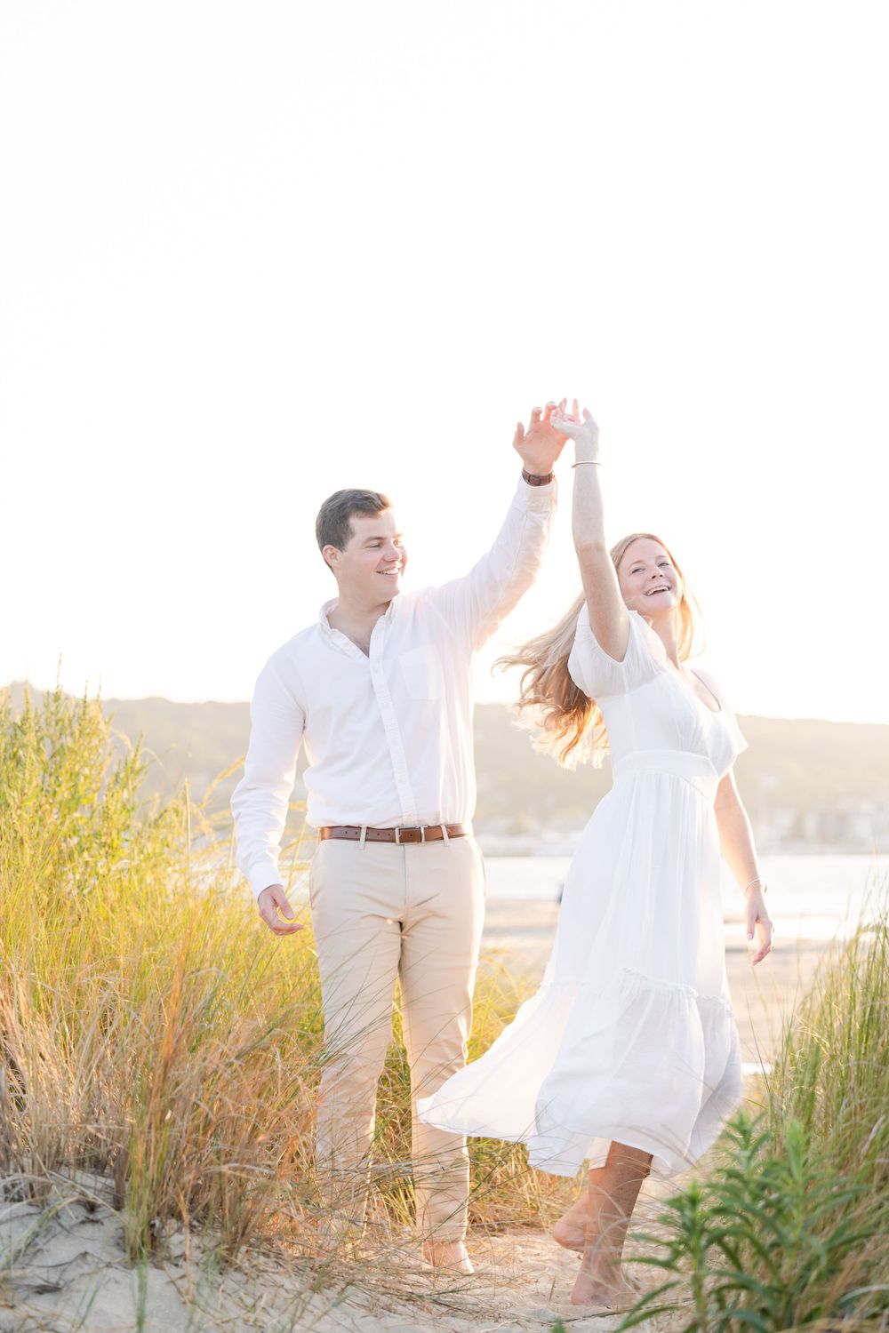 Carefree couple in white outfits dancing and celebrating on a beach at sunset.