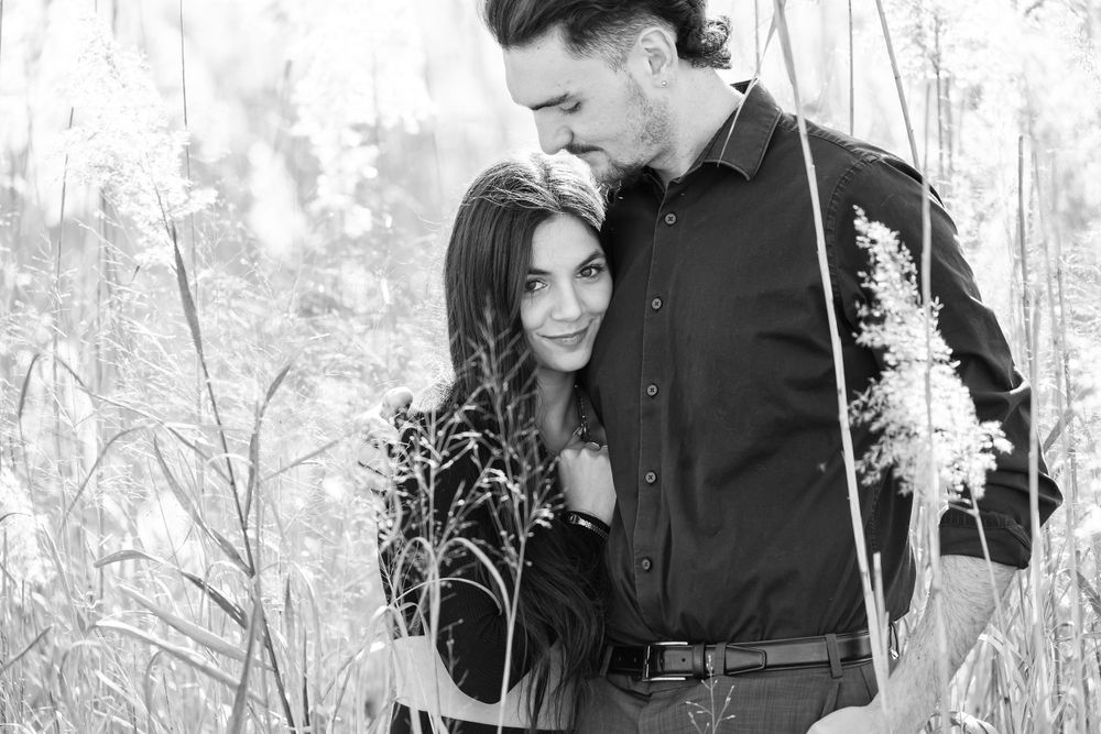 A romantic couple embraces in front of natural tall grass in an outdoor setting during golden hour.