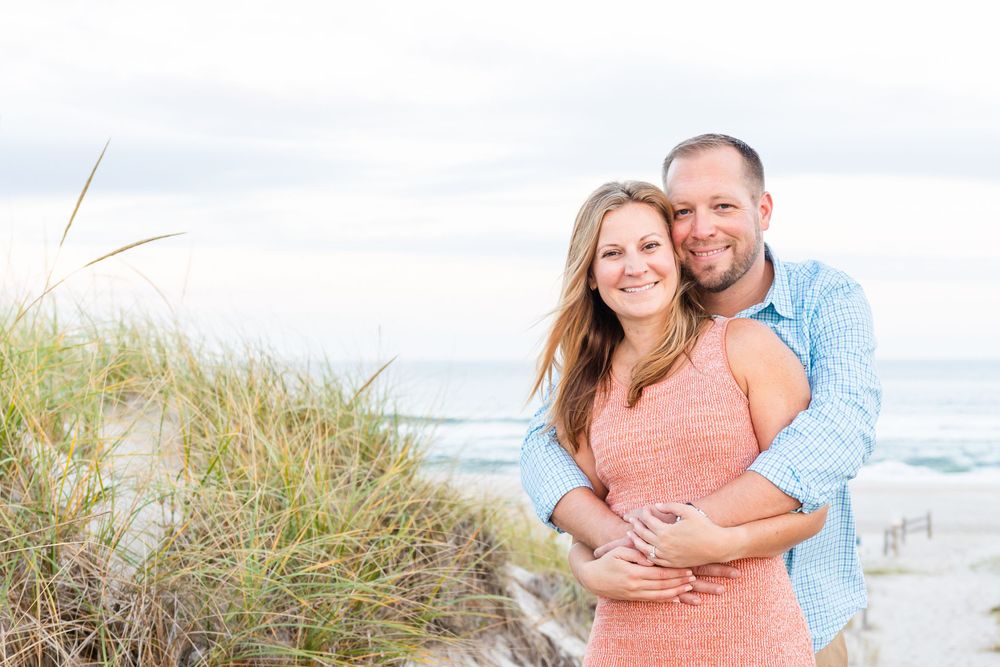 Happy couple embracing on beach with ocean and sand dunes in background.